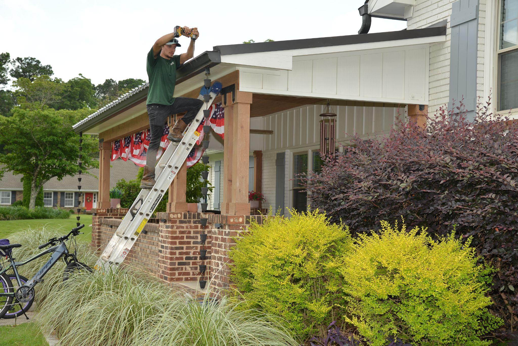Licensed installer securing a new gutter system along an Alabama front porch in July.